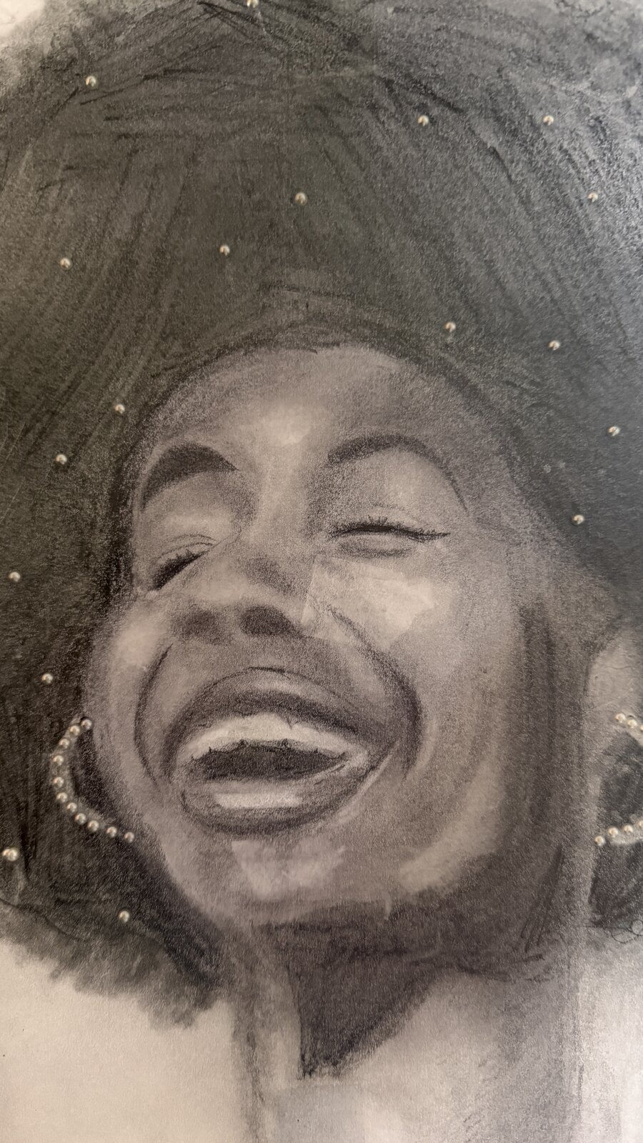 Charcoal drawing by Rosalyn Dearing of a woman laughing with her eyes closed, with real pearls set into her hair and earrings